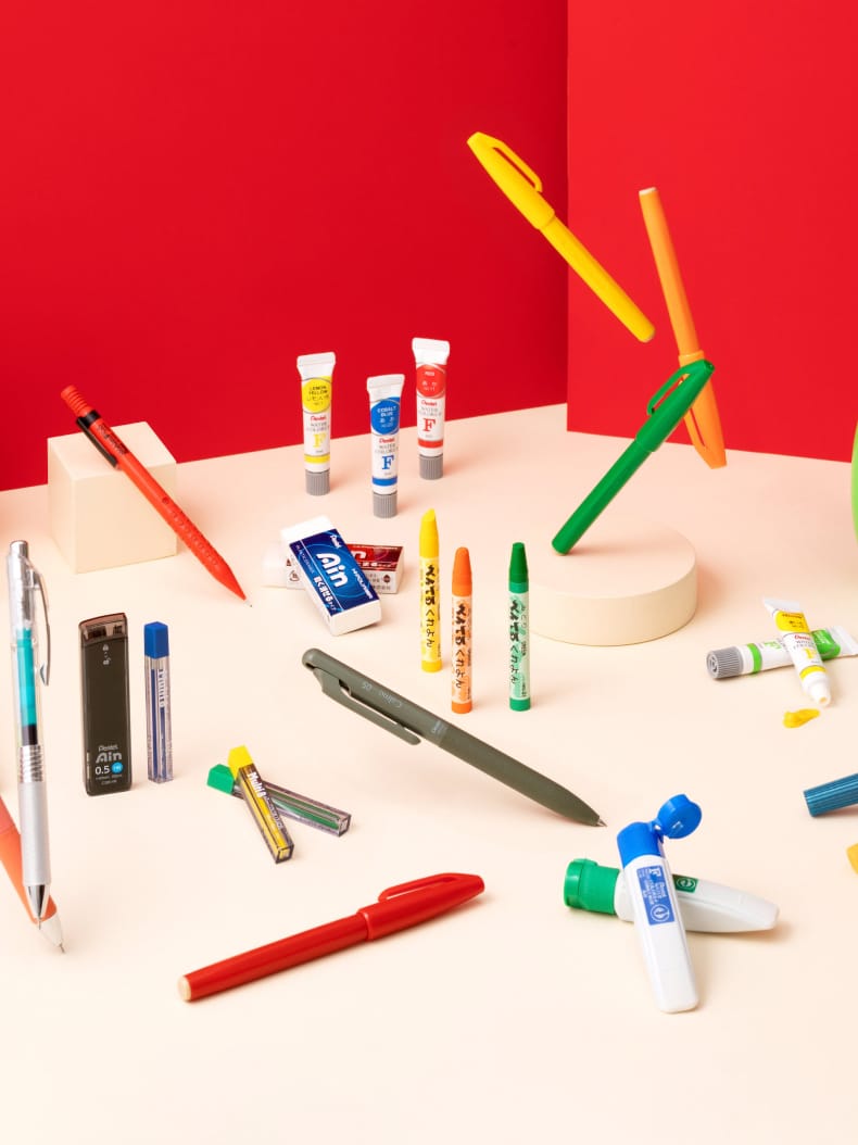 Pentel mechanical pencils, lead, erasers, pens and art materials arranged against a red background